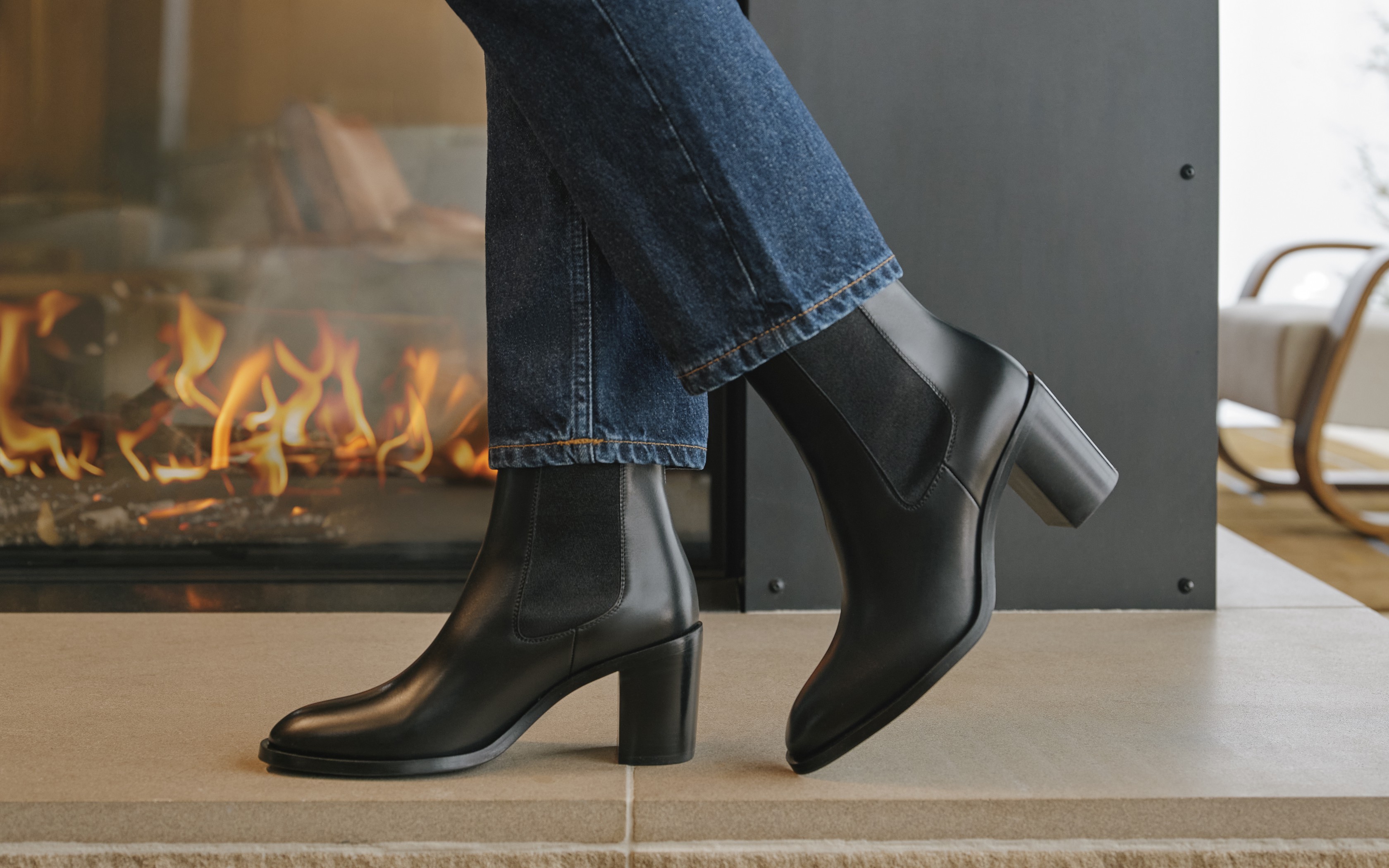Person trägt schwarze Leder-Stiefeletten und blaue Jeans vor einem Kamin.