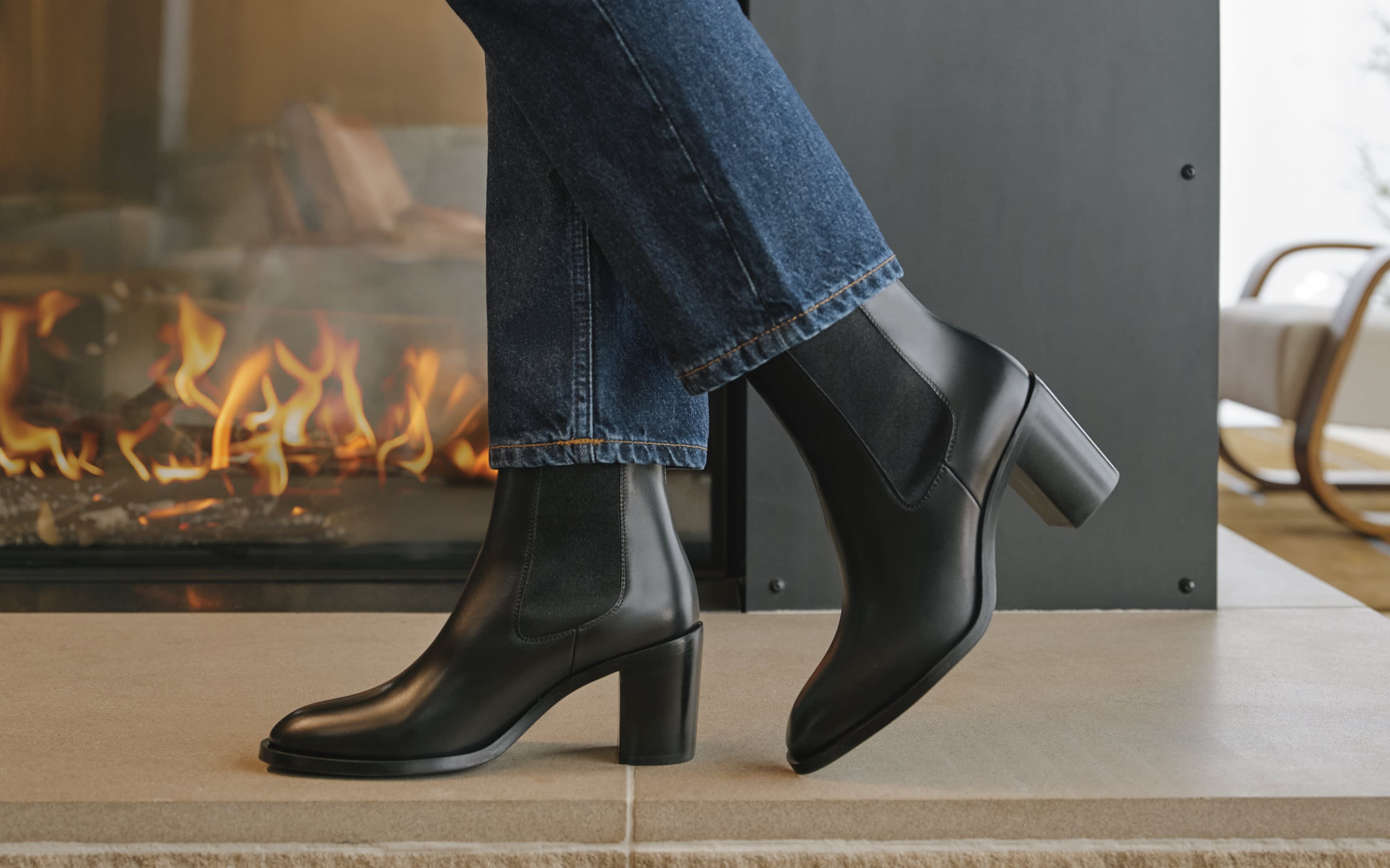 Person trägt schwarze Leder-Stiefeletten und blaue Jeans vor einem Kamin.