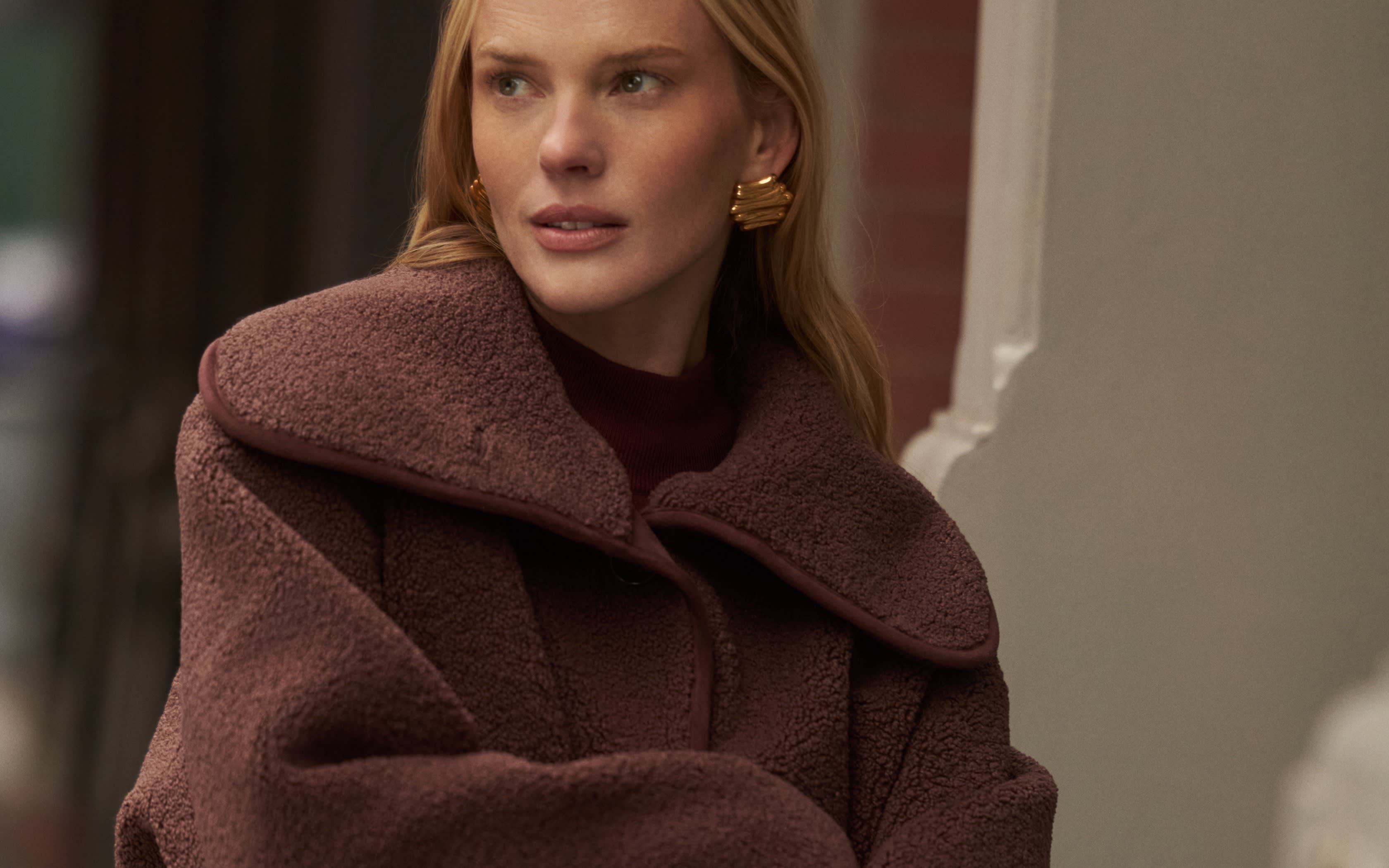 Femme en veste polaire marron et boucles d'oreilles dorées en ville.