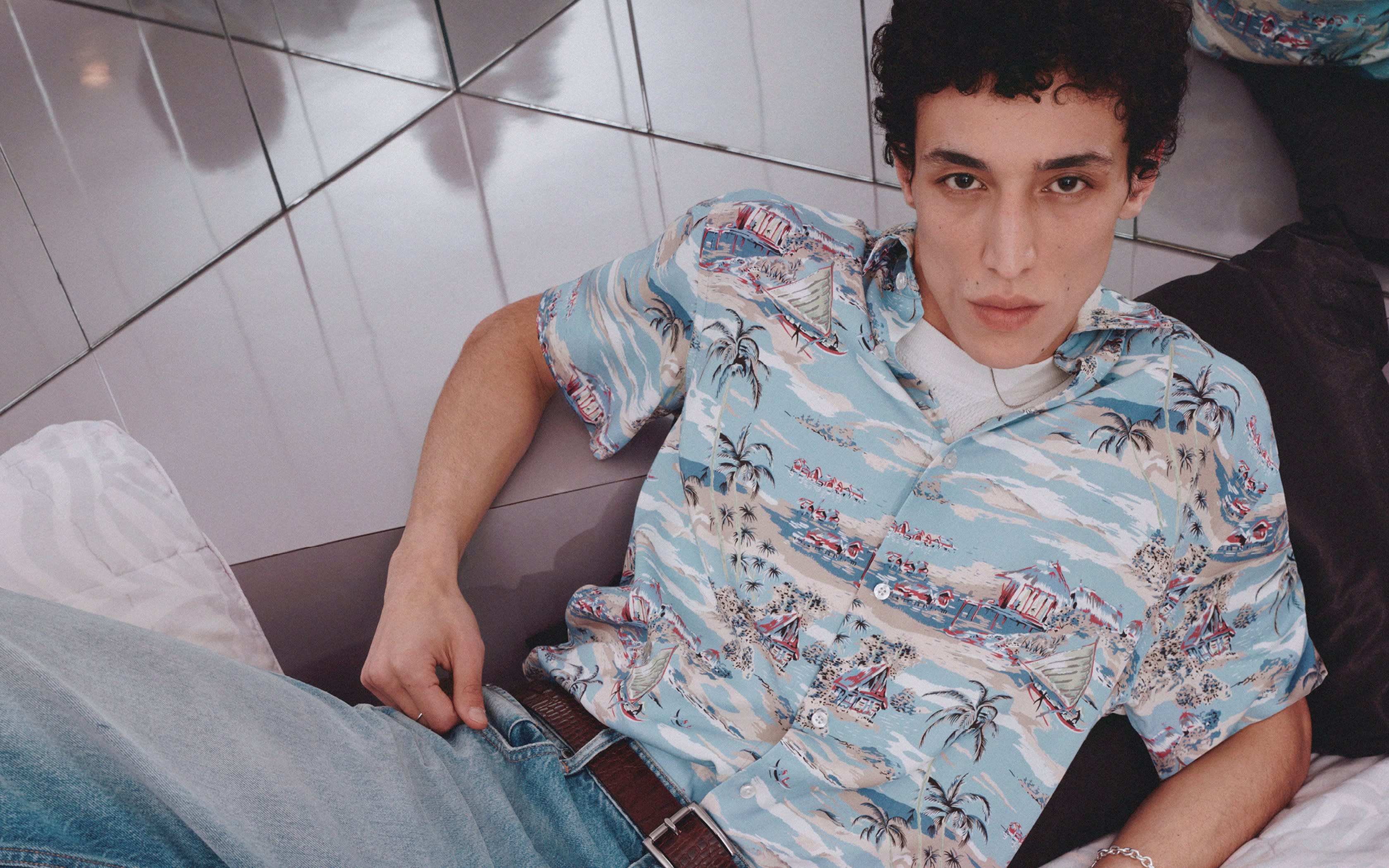 Jeune homme bouclé en chemise tropicale bleu clair et jean.
