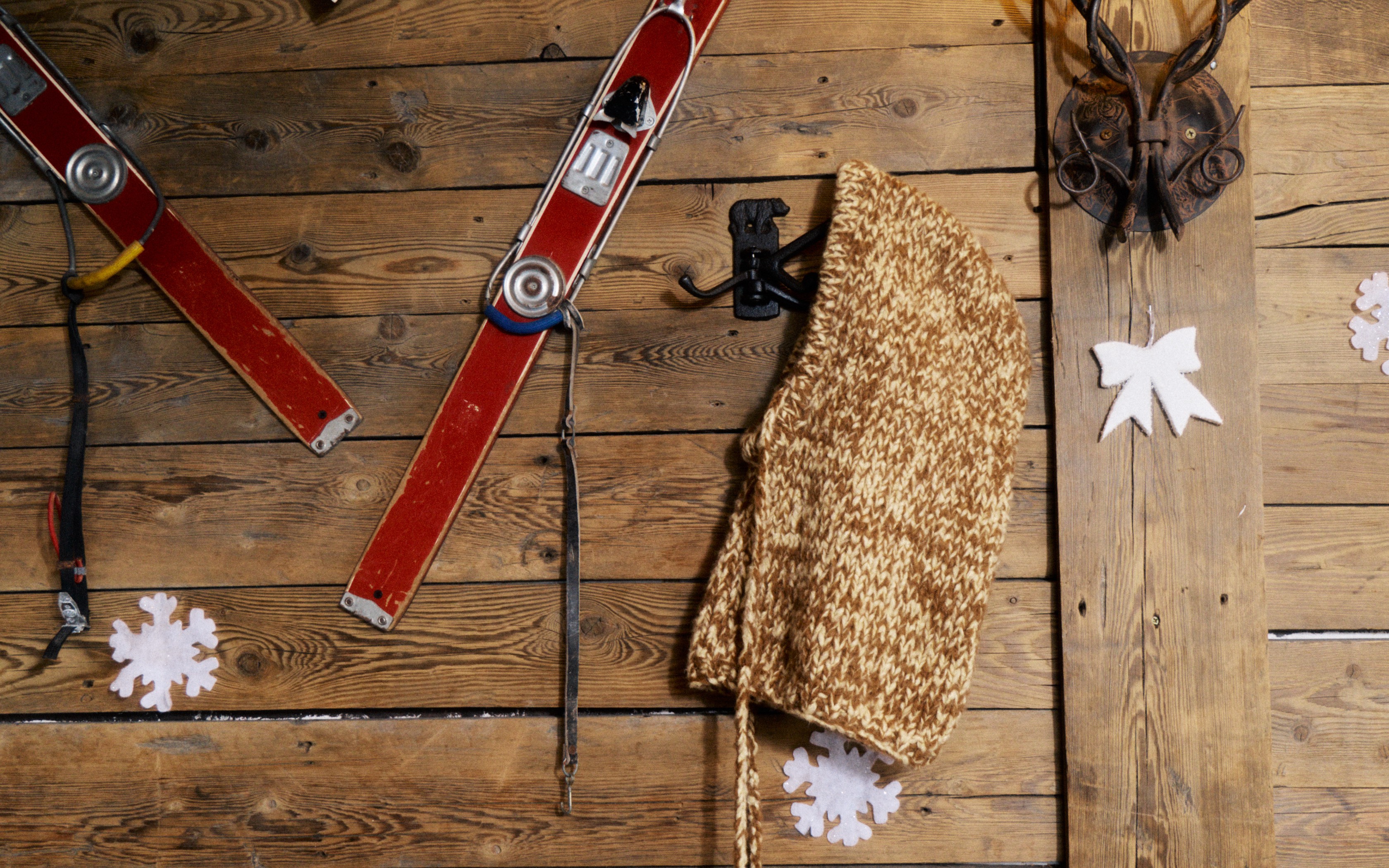 Cagoule tricotée marron sur mur en bois avec des skis rouges