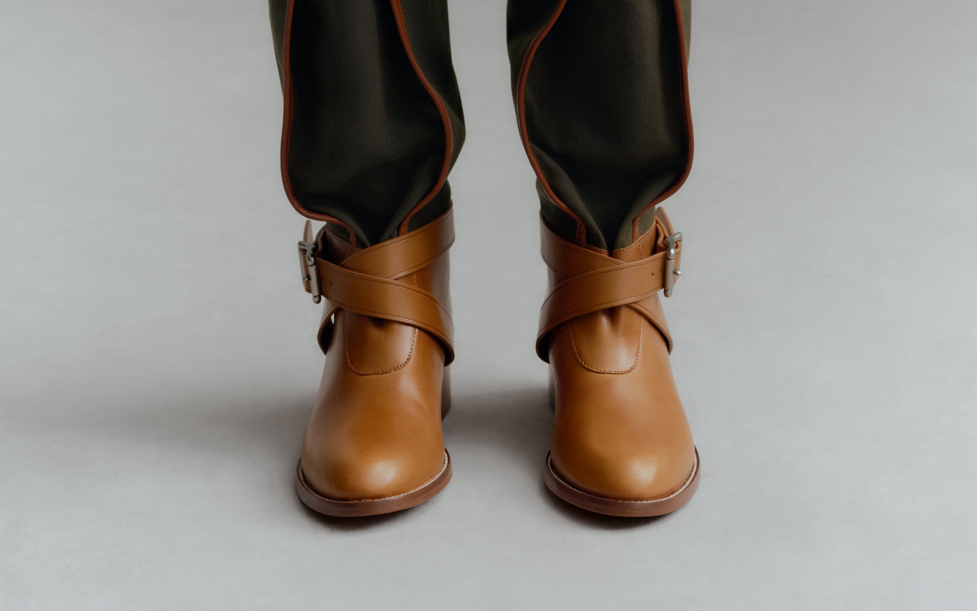 Kniehohe Stiefel aus grünem Stoff mit braunen Lederriemen und Schnallen.