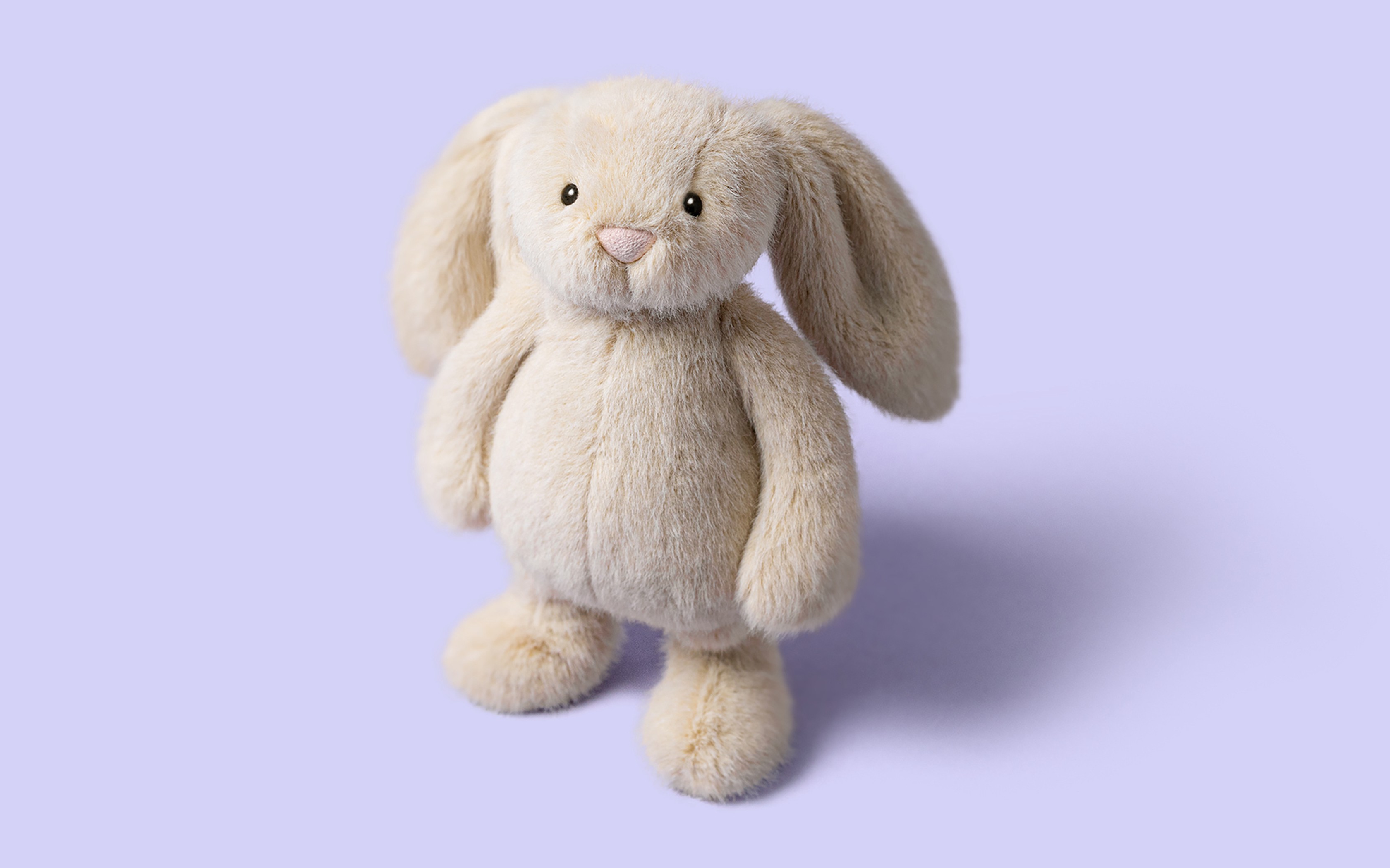 Un lapin en peluche duveteux couleur crème sur fond violet clair.