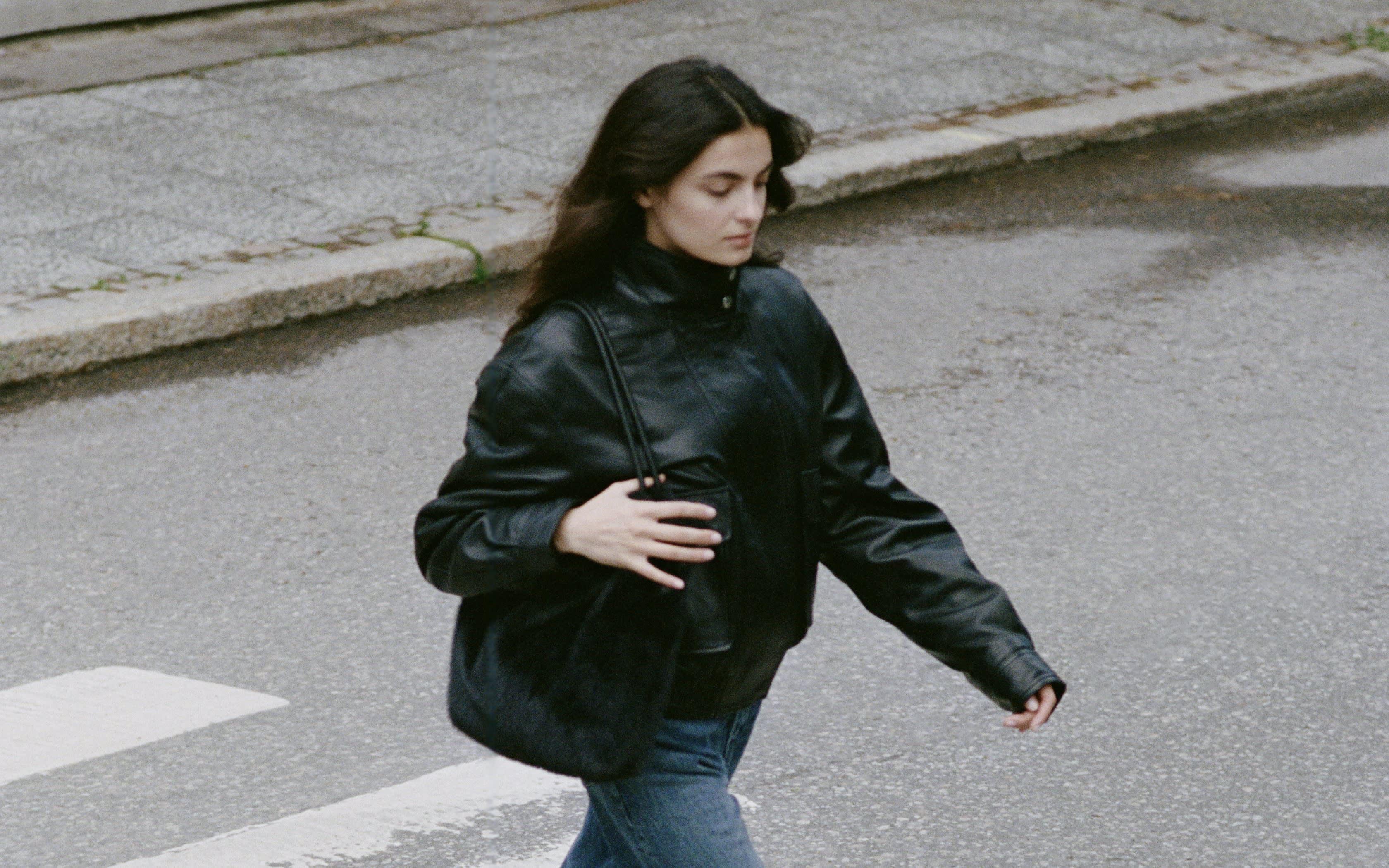 Femme en veste de cuir noire et jean traversant un passage piéton.