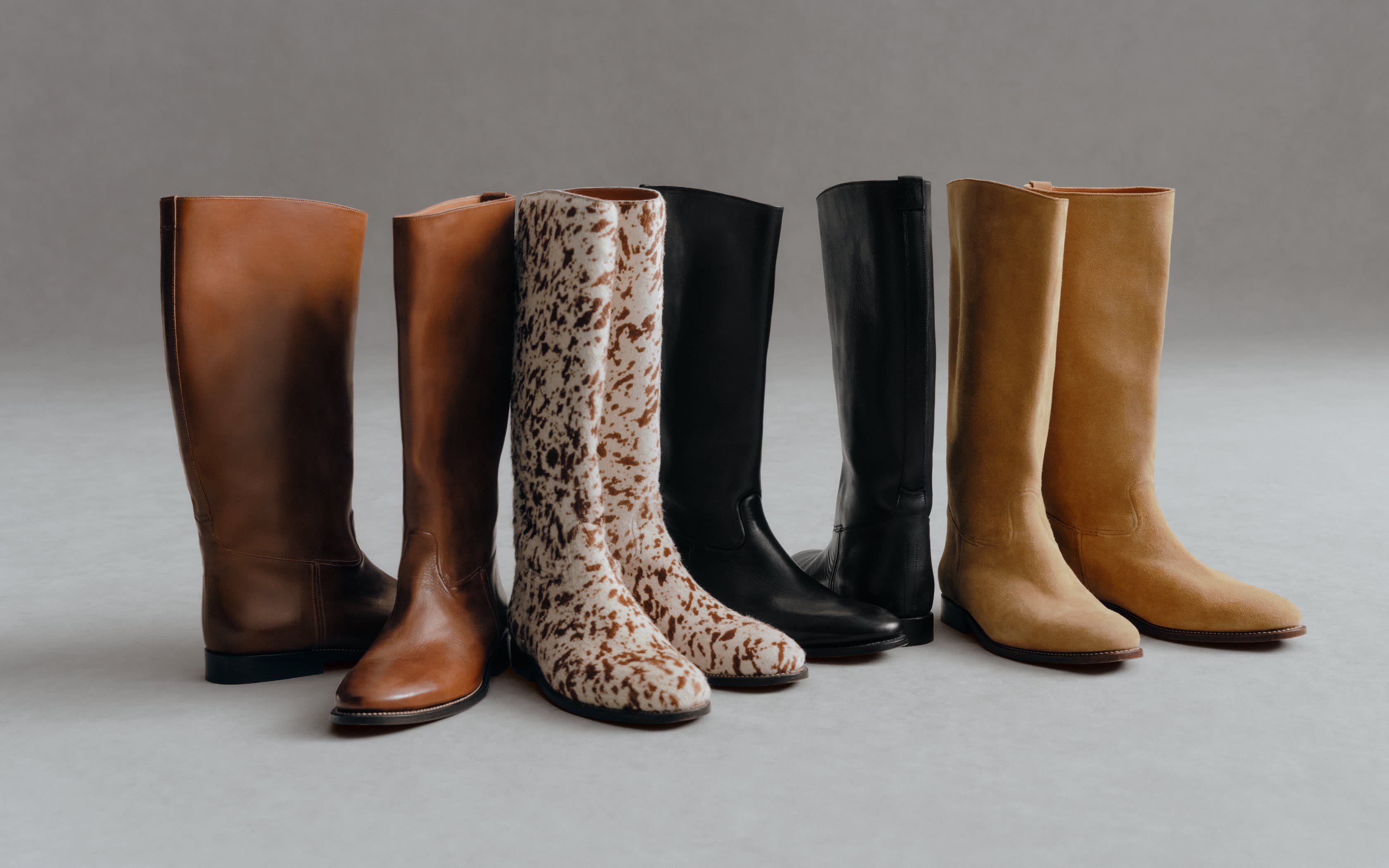Sechs Paar kniehohe Stiefel in Braun, Schwarz, Beige und mit Kuhfell-Muster auf grauem Hintergrund.