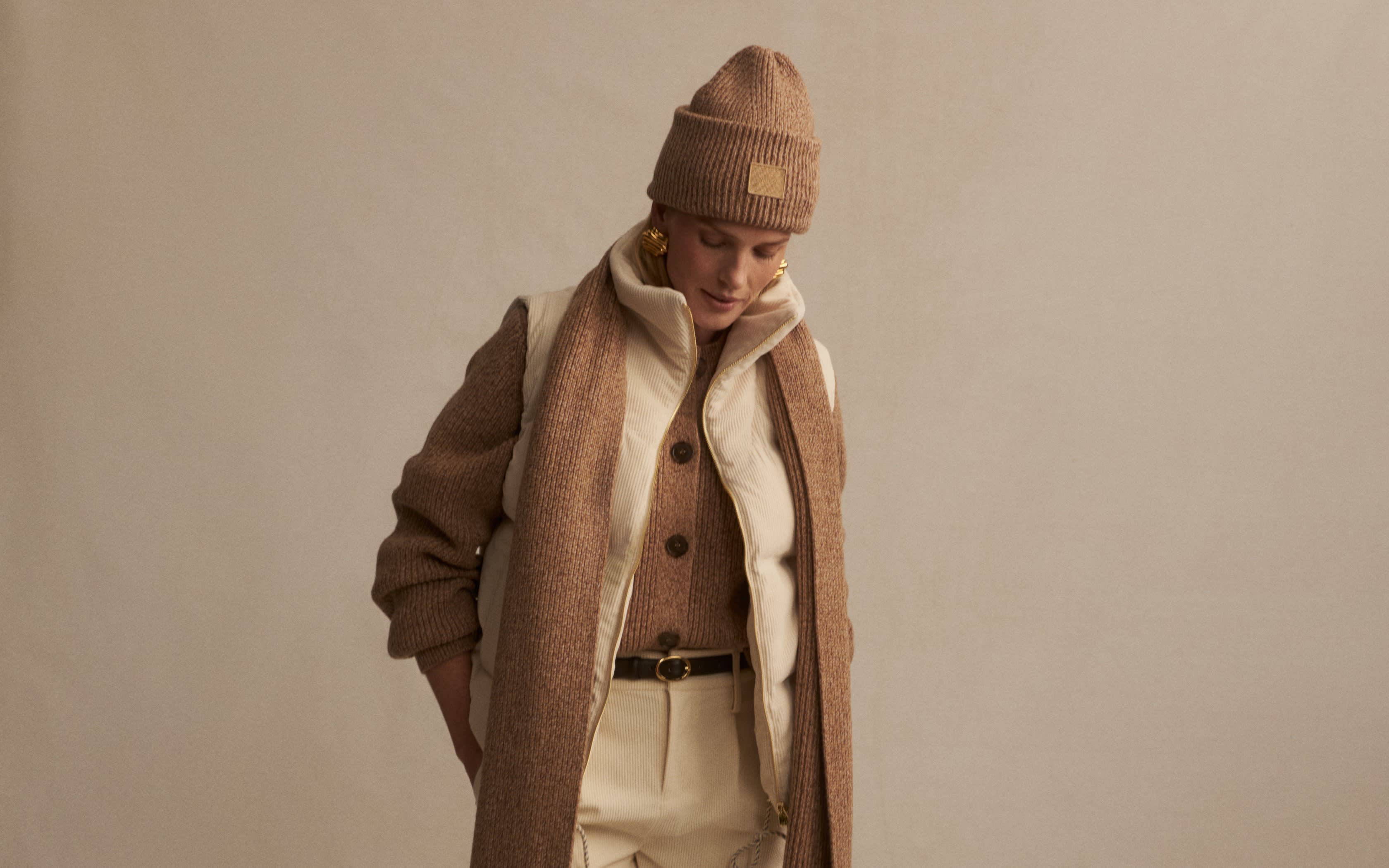Mannequin portant une veste matelassée, un bonnet, une écharpe et un pantalon beige dans un studio.