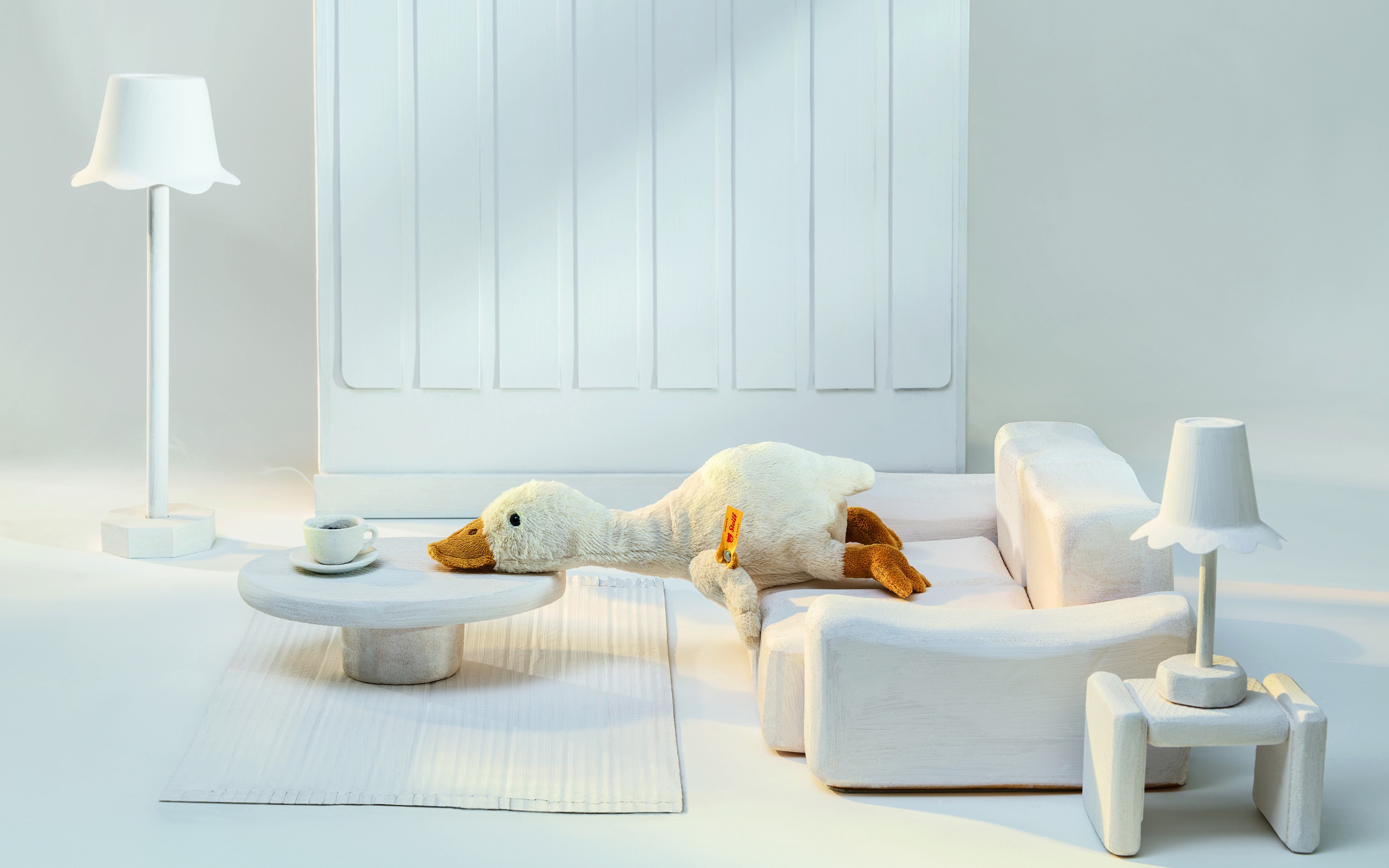 Canard en peluche sur un canapé blanc dans une pièce minimaliste.