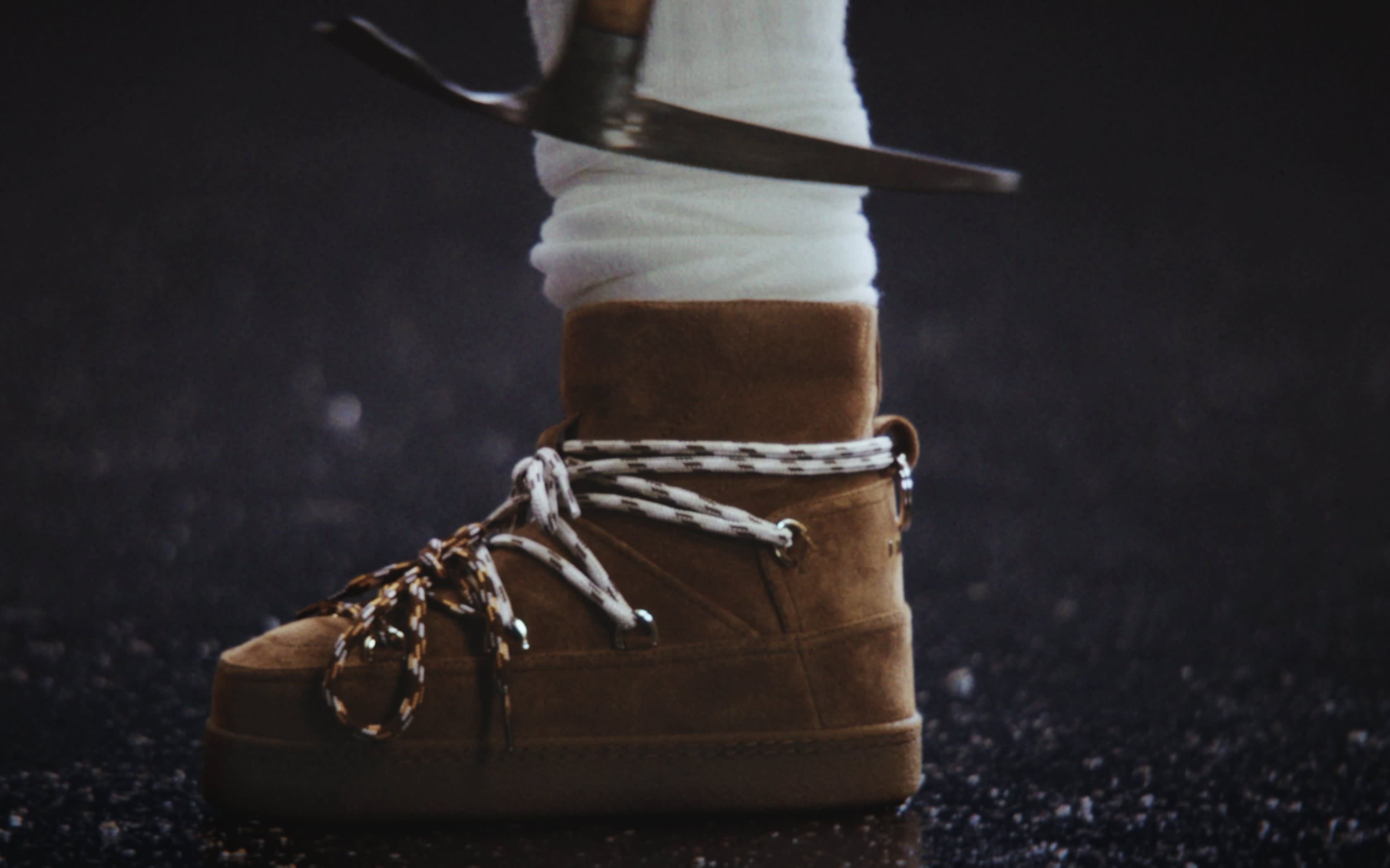 Brauner Wildleder-Winterstiefel mit weißer Schnürung auf dunklem Untergrund.