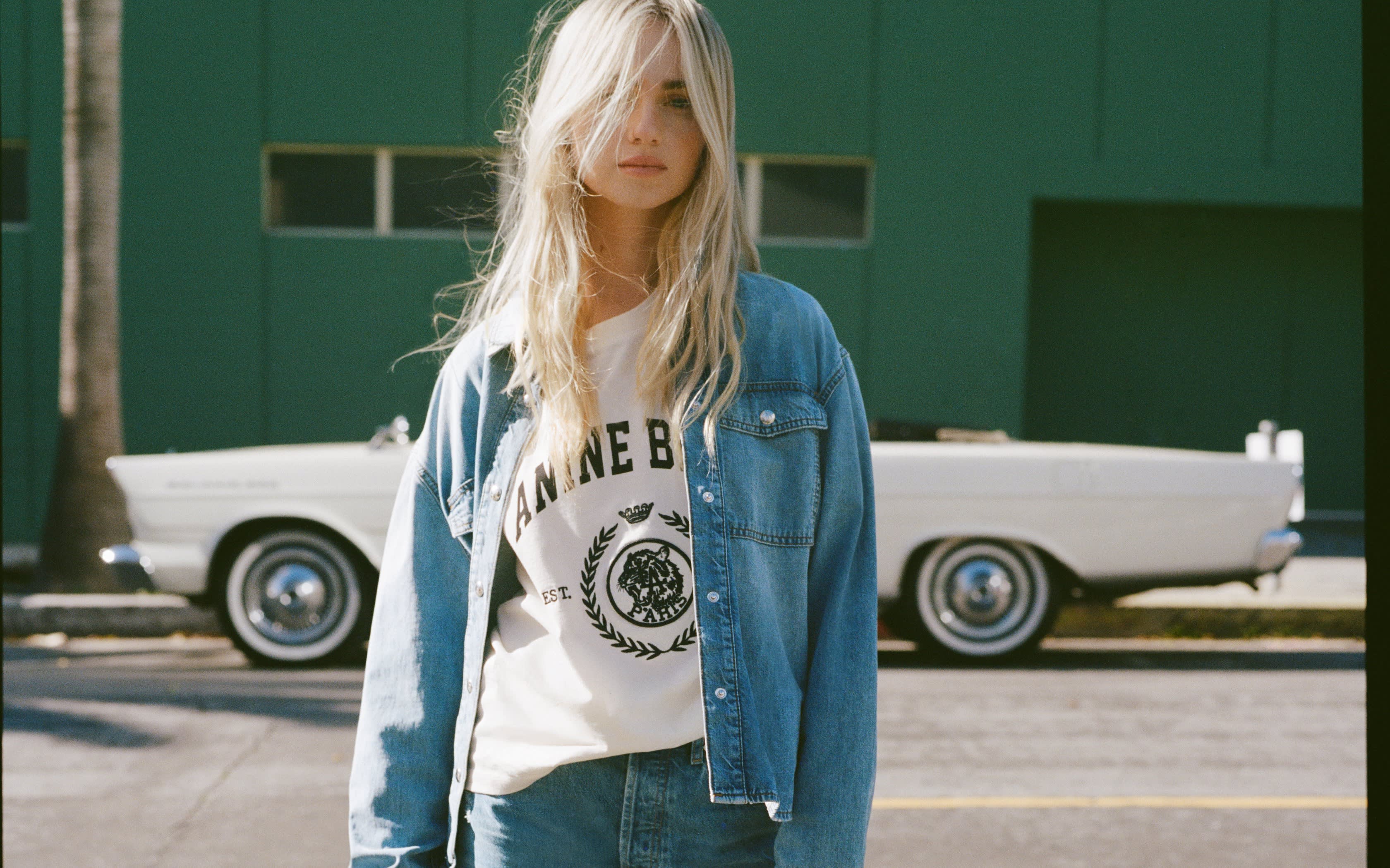 Femme blonde en chemise et pantalon en jean sur un parking ensoleillé.